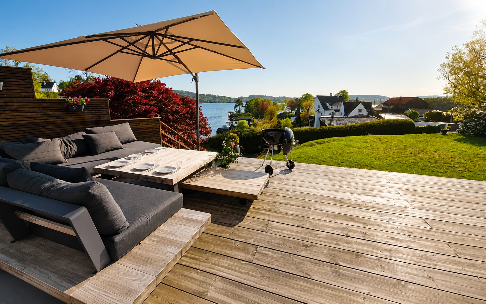 Deck with lounge furniture, parasol and barbecue, water in the background