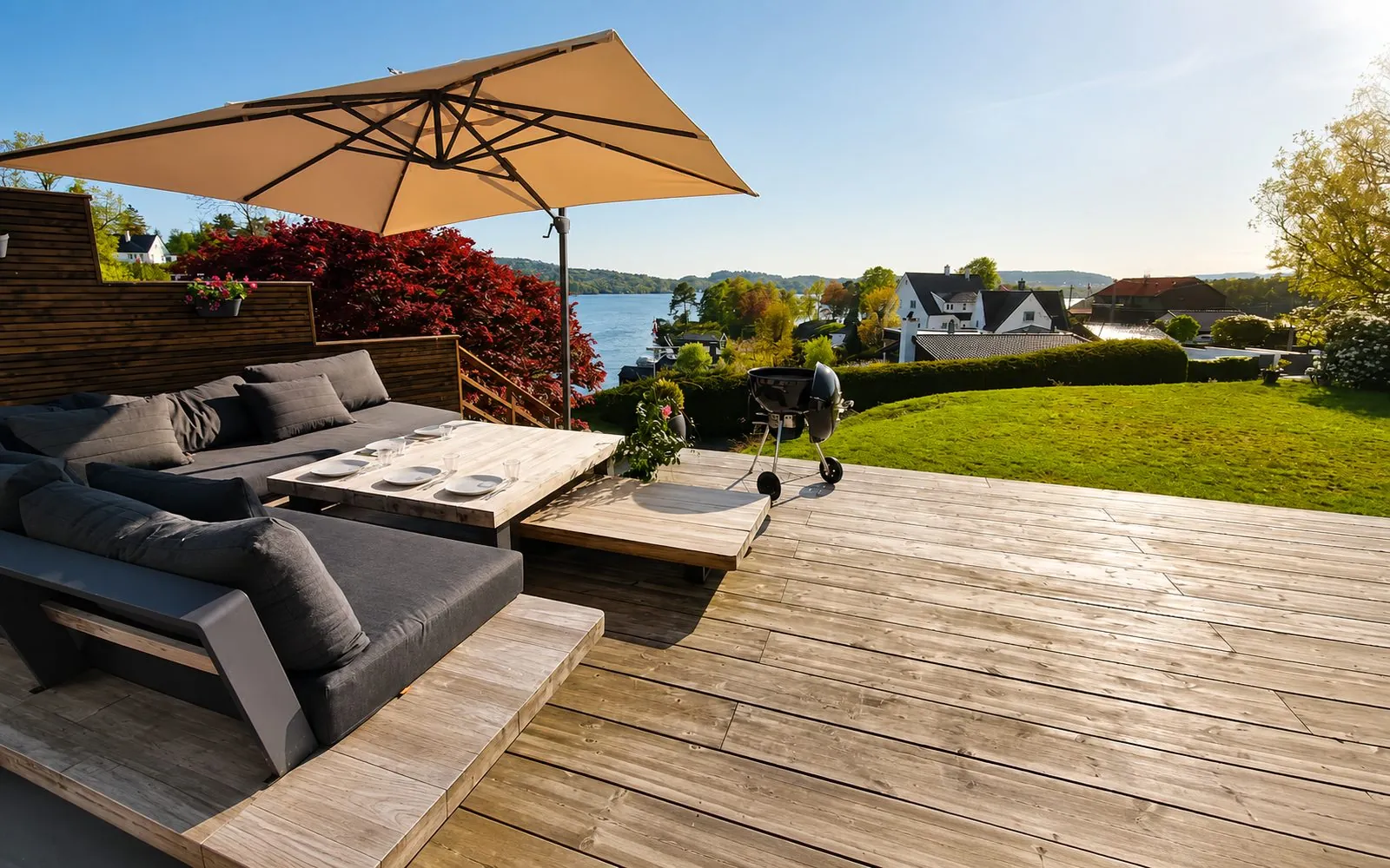 Deck with lounge furniture, parasol and barbecue, water in the background